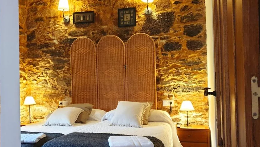 Bedroom of the Inês e Pedro apartment with wicker headboard and lit stone wall